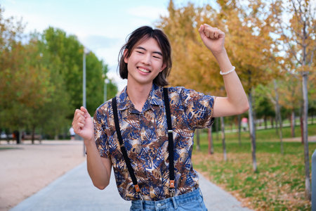 Young Taiwanese man smiling and dancing rock and roll in a park.の写真素材