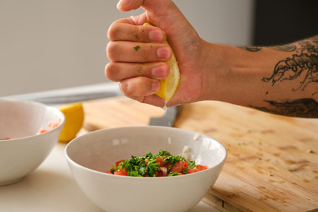 Young unrecognizable tattooed latin man adding lemon to the pico de gallo recipe.の写真素材