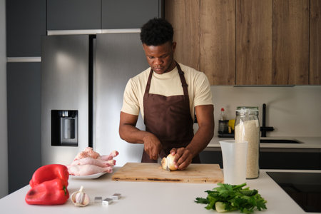 Young black man cutting onion to prepare chicken recipe in a kitchen.の写真素材