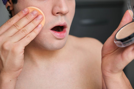 Young unrecognizable transgender man applying make-up base to hide his beard.の写真素材