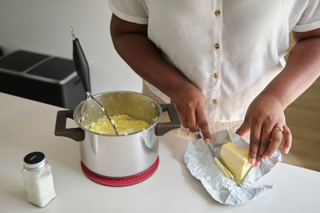 Close up of cuban woman hands adding butter to the mashed potatoes to prepare cuban style stuffed potatoes.の写真素材