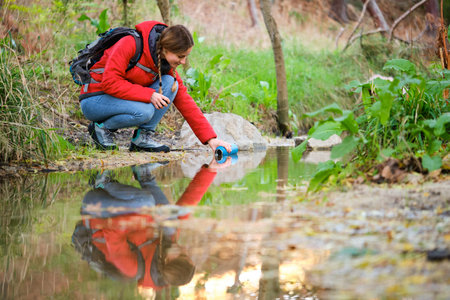 Young female hiker filling canteen of raw water in a creek.