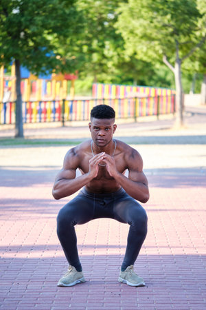 Young fit shirtless black man doing squats outdoors on sunny summer day. Fitness and sport lifestyle.の写真素材