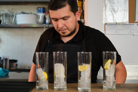 Latin man preparing soft drinks in a glasses with lemon and ice. Restaurant or bar.