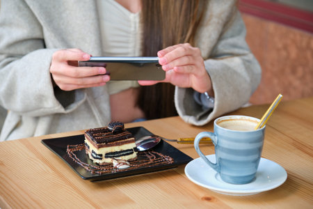 Unrecognizable woman taking a photo of a cake with her smartphone before eating it in cafe.の写真素材