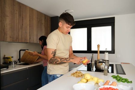 Two young latin people peeling potatoes and washing chopping board to prepare a recipe at kitchen.