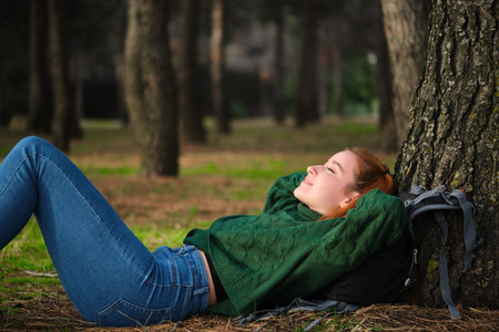 Redhead young woman resting lying under tree in forest. Relaxing in nature.の写真素材