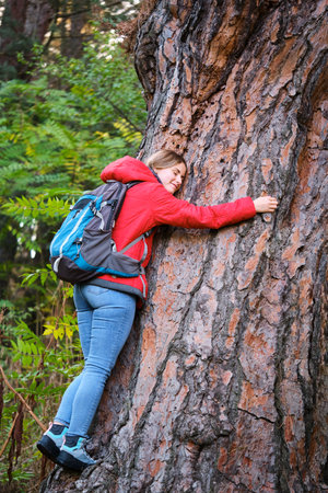 Smiling young female trekker hugging a big tree in the forest.の写真素材