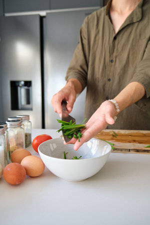 Unrecognizable asian young man putting chopped chinese chive in a bowl at kitchen.の写真素材