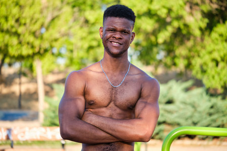 Portrait of a young fit shirtless black man smiling arms crossed looking at camera in a park outdoors. Fitness and sport lifestyle.の写真素材
