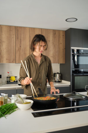 Smiling asian young man cooking chinese or taiwanese tomato scrambled eggs at kitchen.の写真素材