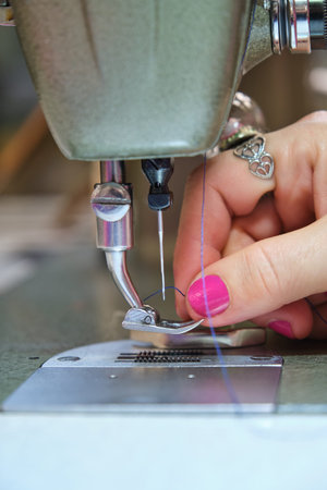 Close up of a dressmaker hand threading sewing machine in a sewing workshop.