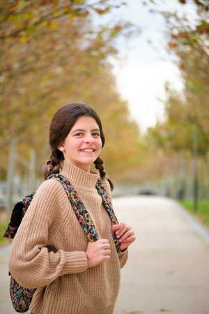 Preteen girl with two braids and backpack smiling and looking at camera outdoors in autumn. Back to school.の写真素材