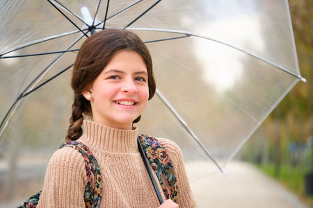 Preteen girl with an umbrella and backpack smiling and looking at camera outdoors in autumn. Back to school.の写真素材