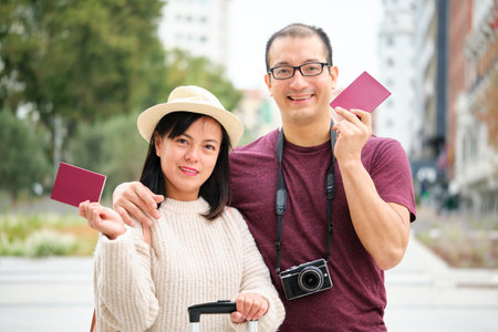Multiracial couple of tourists smiling, holding passports and looking at camera. Sightseeing in Madrid, Spain.の写真素材