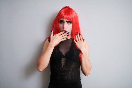 Portrait of drag queen amazed wearing a red wig and looking at camera on grey background. LGBTQ...
