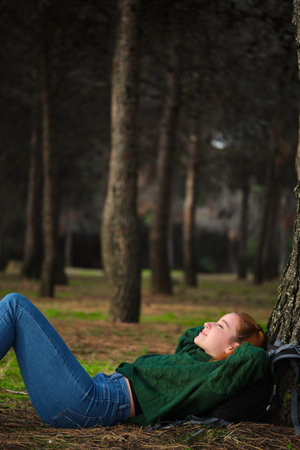 Redhead young woman resting lying under tree in forest. Relaxing in nature.の写真素材