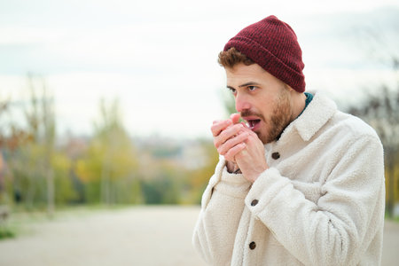Latin young man rubbing his hands to warmth during winter. Cold weather. Flu.の写真素材