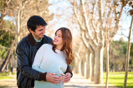 Happy pregnant couple embracing and touching her belly looking each other in a park. Pregnancy.の写真素材