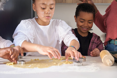 Close up of cousins cutting cookie shapes in a cookie dough in the kitchen with their family.の写真素材