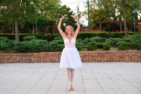 Mature smiling woman dancing ballet in a park at street.の写真素材