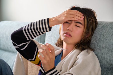 Sick taiwanese man taking his temperature with a thermometer. Fever, flu, illness concepts.