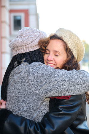 Two multiracial female happy friends hugging each other and smiling on city street.の写真素材