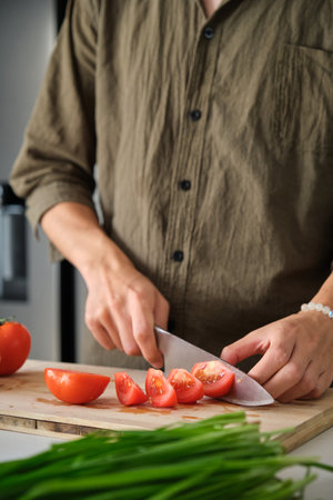 Unrecognizable young man cutting tomatoes on a chopping board at kitchen.の写真素材