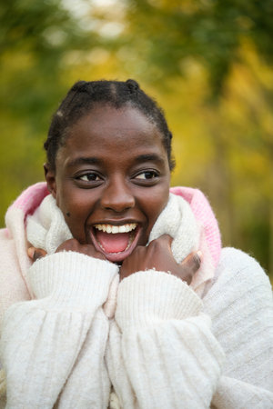 Portrait of an african woman screaming and covering up with a scarf in autumn.の写真素材