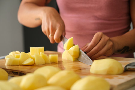 Young unrecognizable tattooed latin woman cutting potatoes at kitchen to prepare a recipe.の写真素材