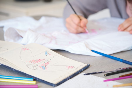 Unrecognizable woman painting a floral design in a white shirt. Unique clothing designs.の写真素材