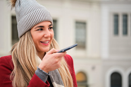 Young caucasian blonde woman recording voice message on the smart phone on the street in winter.