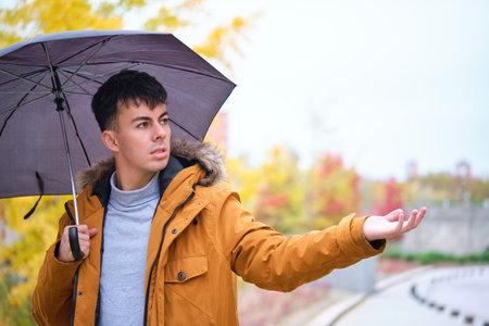 Young man holding an umbrella and checking if it is still raining in an autumn day at the street.の写真素材