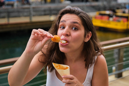 Tourist eating mitarashi dango, traditional Japanese rice dumplings smothered in a sweet soy glaze, and looking at camera at street.の写真素材