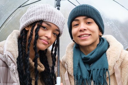 Happy dominican lesbian couple with an umbrella at street in a rainy day of winter.