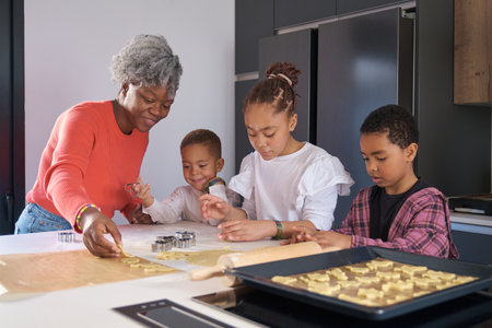 Happy african mother and children cutting cookie shapes in a cookie dough in the kitchen.の写真素材