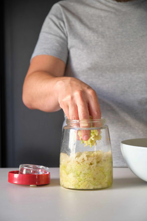 Unrecognizable man putting cabbage into the fermentation jar to prepare homemade sauerkraut.