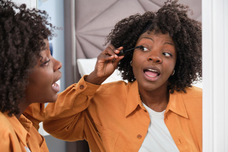 Happy african woman applying mascara in front of the mirror.の写真素材