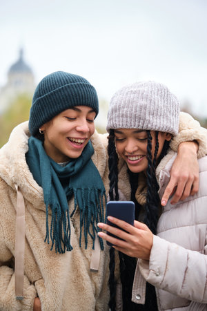 Happy dominican lesbian couple using the smartphone at street in winter.の写真素材