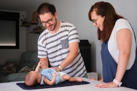 Happy Caucasian parents changing their one month daughter diaper at home. Baby girl care.の写真素材
