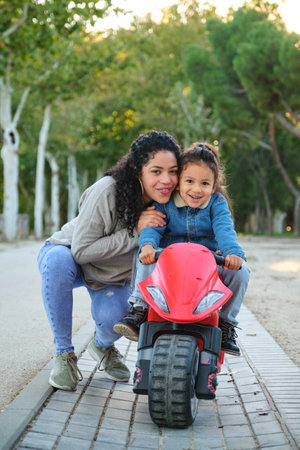 Happy Latin mother hugging her son on a balance bike in a park. Latin family.の写真素材