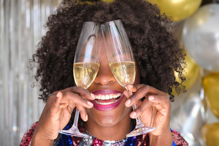 African woman with two glasses of champagne on her eyes celebrating New Year at a New Years Eve party.の写真素材
