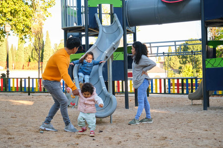 Hispanic parents playing with her children at the slide in a park. Latin family.の写真素材