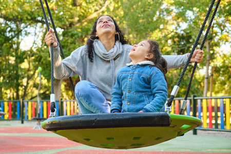 Happy Latin mother playing with her son looking up on a swing in a park. Latin family.の写真素材