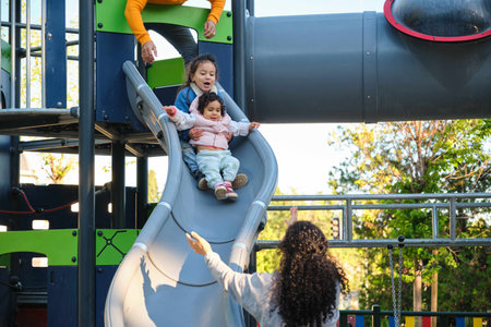 Hispanic parents playing with her children at the slide in a park. Latin family.の写真素材