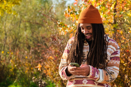 African American young man with dreadlocks happy using the smartphone in a sunny day of autumn.の写真素材