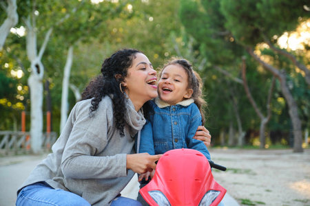 Dominican mother and son hugging and laughing on a balance bike in a park. Latin family.の写真素材