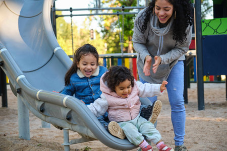 Happy Dominican mother playing with her children at the slide in a park. Latin family.の写真素材