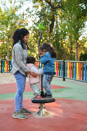 Happy Dominican mother playing with her children at the synchro spinner in a park. Latin family.の写真素材
