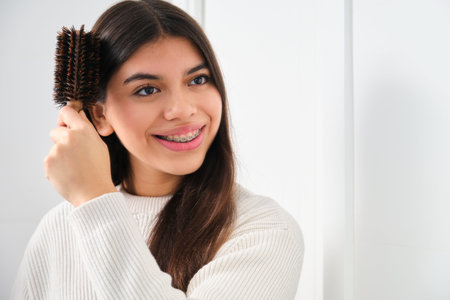 Female Latin teenager with braces brushing her hair in front of the mirror.の写真素材
